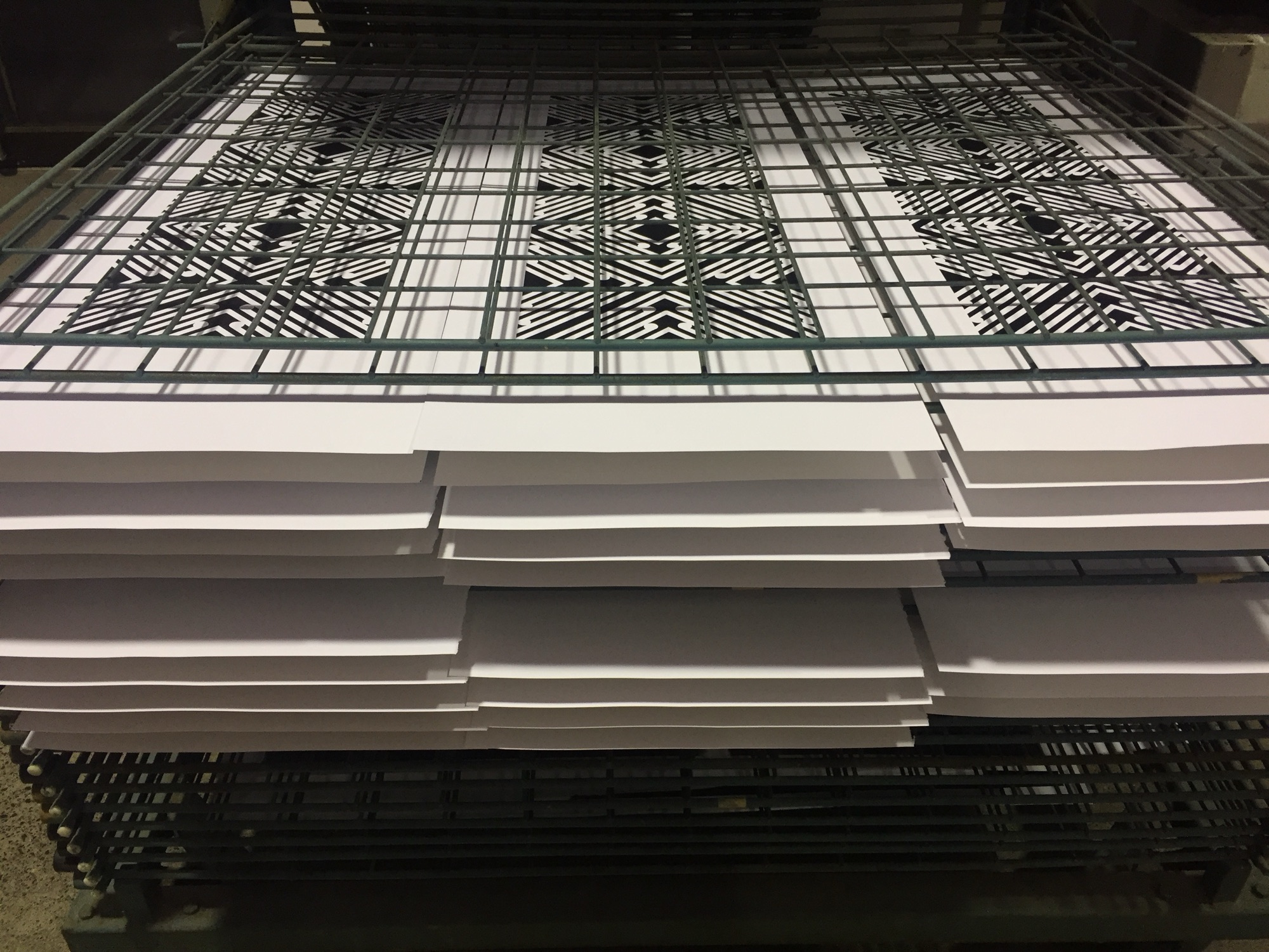 A tall stack of freshly printed sheets with a geometric pattern, drying in the studio