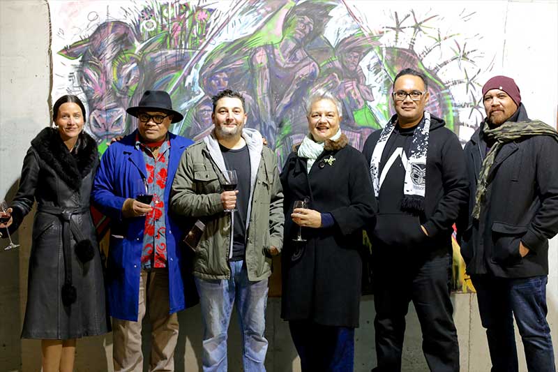Artists of the Barrel Store Colony group show standing in front of a large mural